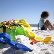 Beach bag, beach toys and a little girl on the beach.